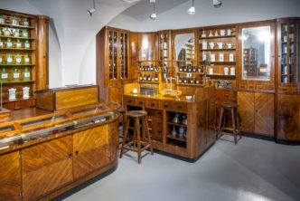 wnętrze starej apteki, drewniany kontuar, drewniane gabloty, w gablotach ceramiczne i szklane fiolki na leki
