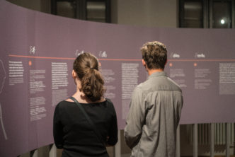 dwie osoby stojące tyłem czytające plansze z napisami na wystawie