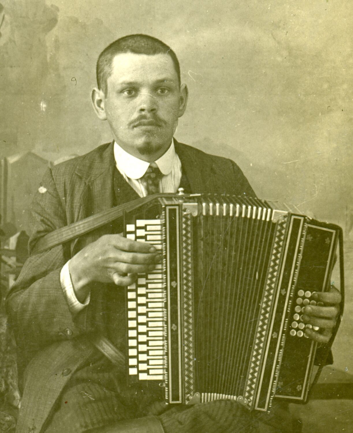 Czarno białe zdjęcie mężczyzny w garniturze trzymającego akordeon.