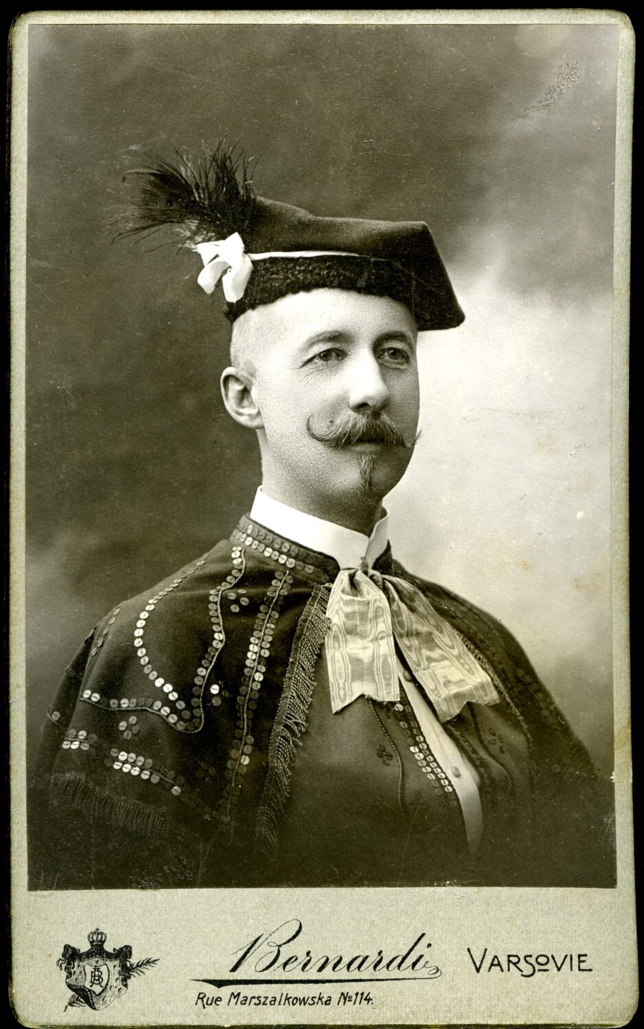 Czarno białe zdjęcie mężczyzny w tradycyjnym stroju ludowym w czapce z piórem.