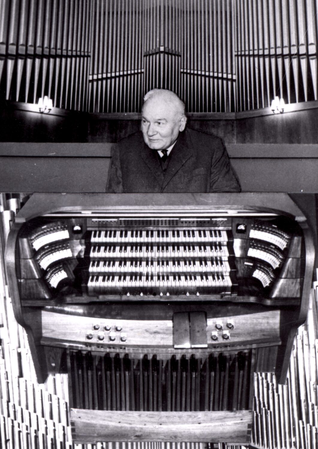 Czarno białe zdjęcie. Starszy mężczyzna siedzący za klawiaturą i na tle organów.