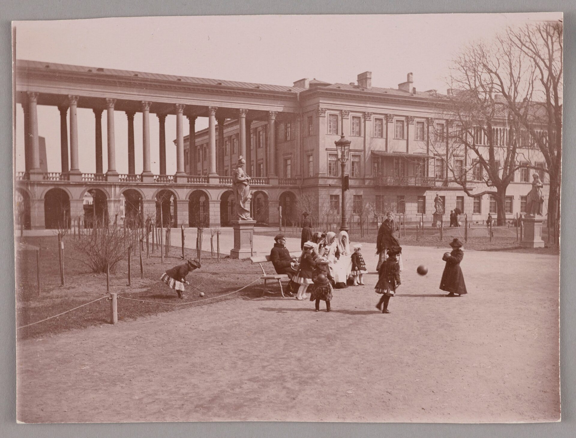 Czarno białe zdjęcie dzieci bawiących się w parku. W tle Pałac Saski.