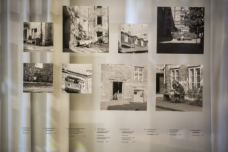 fragment wystawy: zdjęcia na szybie, poniżej opisy zdjęć, w tle ściana i zasłony