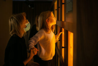dziewczynka zagląda do gabloty oświetlonej jasnym światłem w ciemnym pokoju, kobieta podtrzymuje dziewczynkę za rękę