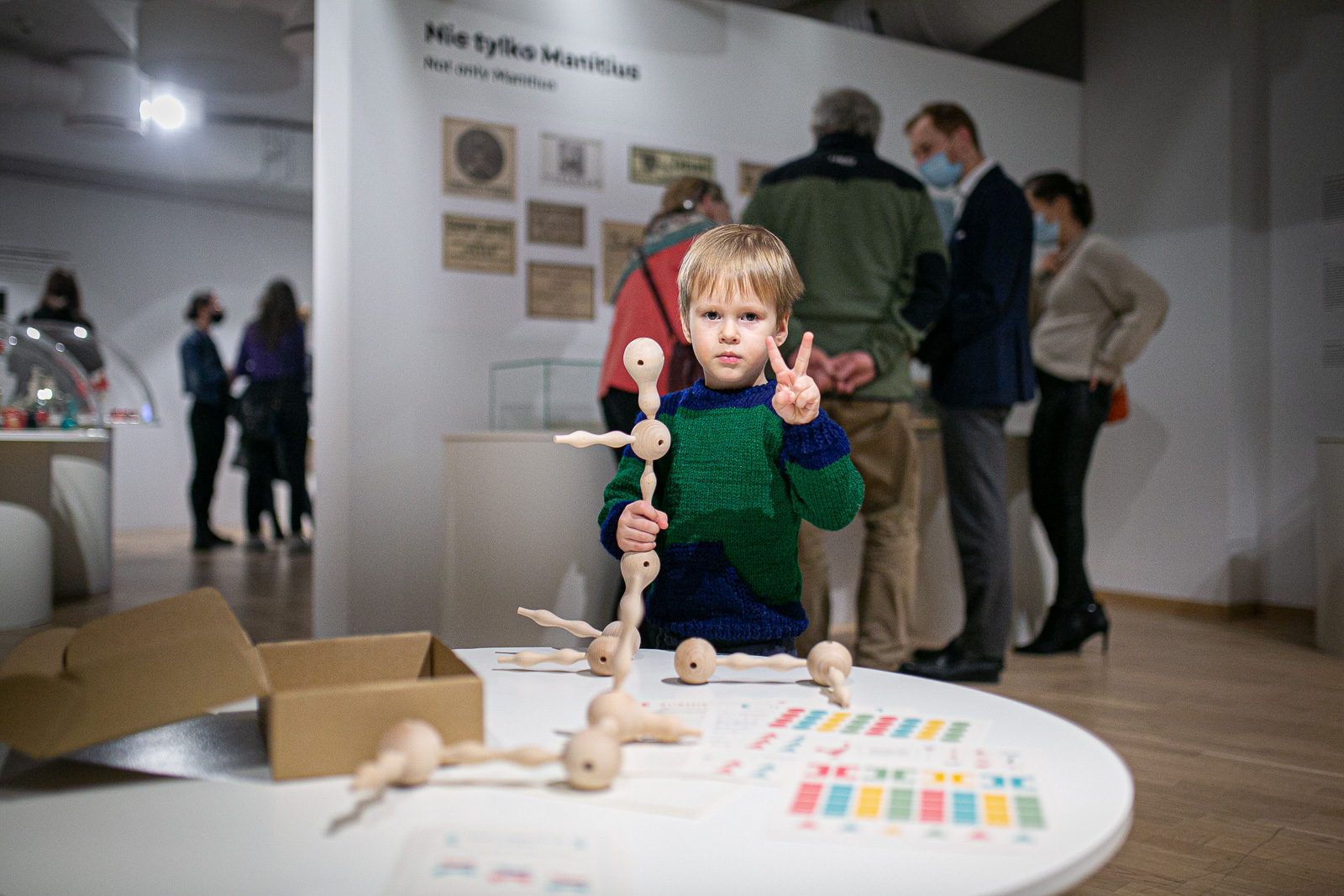 chłopiec na wystawie bawi się drewnianą zabawką, w tle zwiedzający wystawę