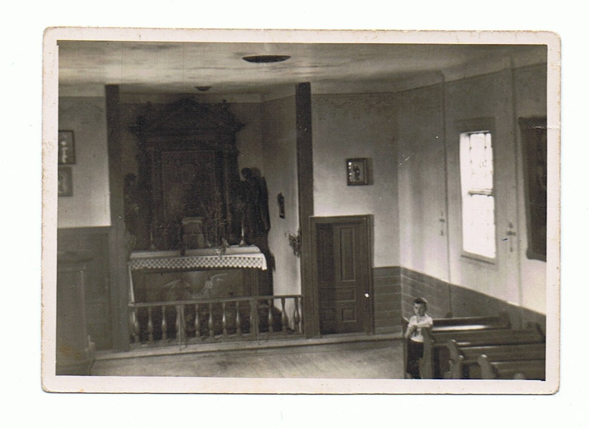 Czarno-białe zdjęcie z wnętrzem kościoła. Ołtarz z obrazem Matki Boskiej. Chłopiec opiera się o ławkę.