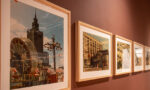 W drewnianych ramkach kolorowe zdjęcia Warszawy na brązowej ścianie.