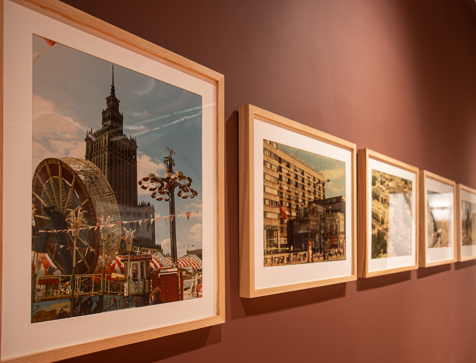 W drewnianych ramkach  kolorowe zdjęcia Warszawy na brązowej ścianie.