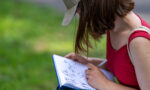 Zdjęcie. Pochylona nad notatnikiem dziewczyna rysuje zwierzęta.