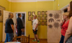Zdjęcie. Grupa osób w pomieszczeniu willi Żabińskich. Przewodnik pokazuje ręką jeden z obrazków na ścianie. Grupa słucha.