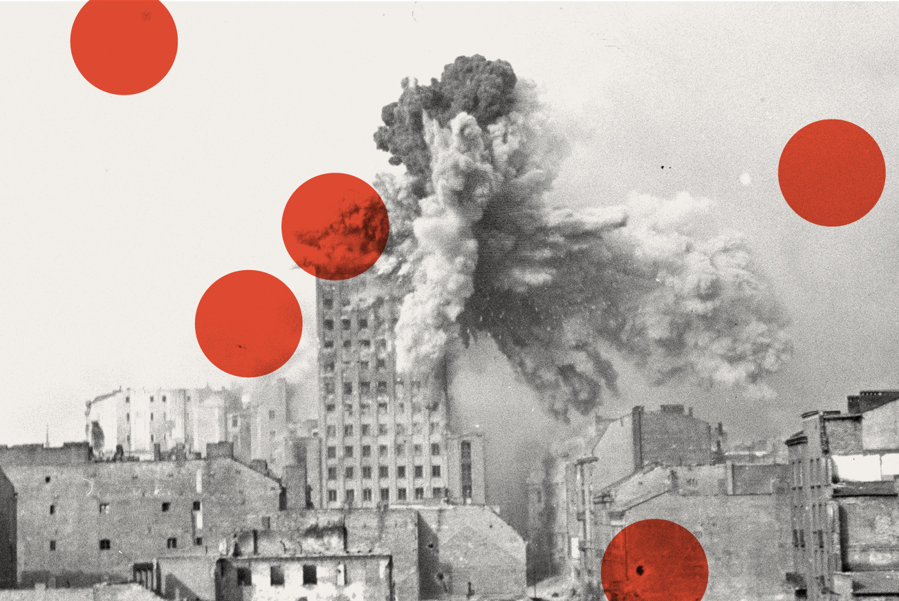 Czarno-białe zdjęcie wybuchającego wieżowca podczas powstania warszawskiego. Nałożone kilka dużych czerwonych kropek.